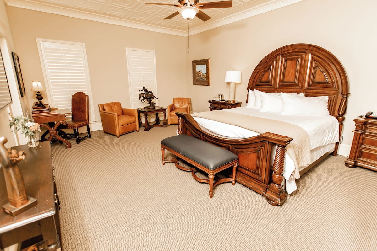 A hotel room with a large bed, a wooden bench, a desk with a lamp, and a chair.