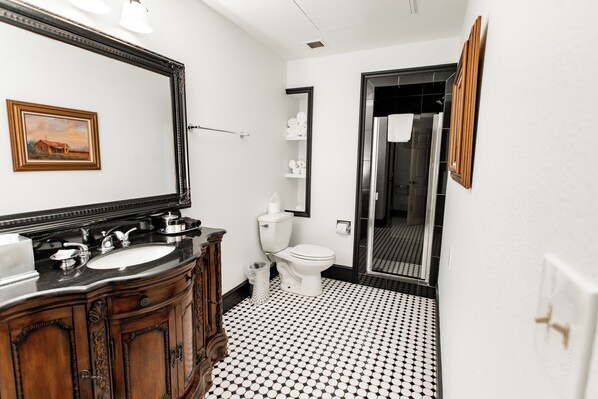 A bathroom with a black and white tiled floor, a wooden vanity with a mirror, a sink, and a toilet.