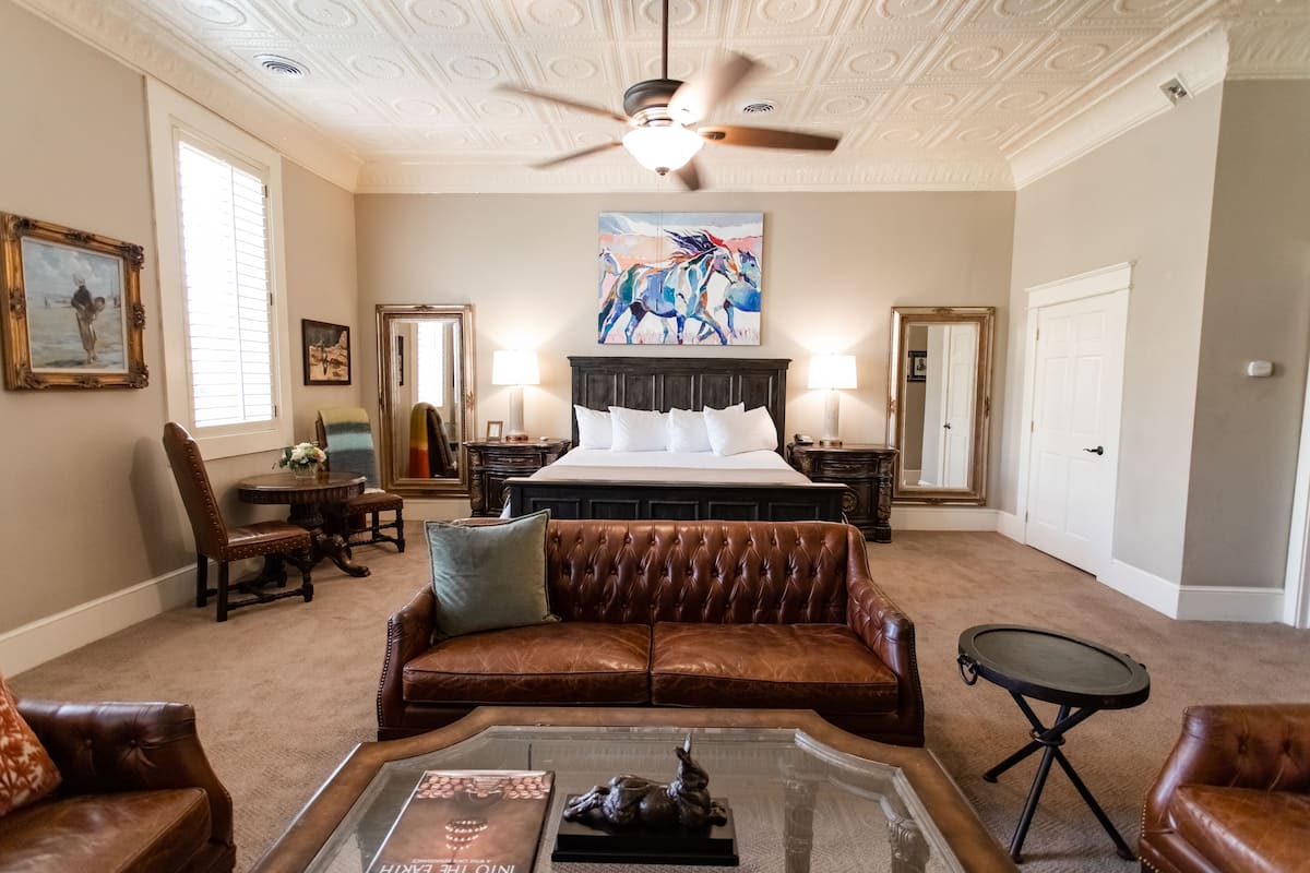 A spacious bedroom with a large bed, a leather sofa, a coffee table, and a ceiling fan.