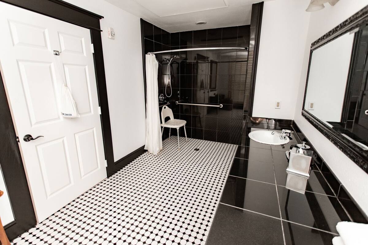 Casa de banho com chão em azulejos, lavatório branco, espelho e área de duche.
