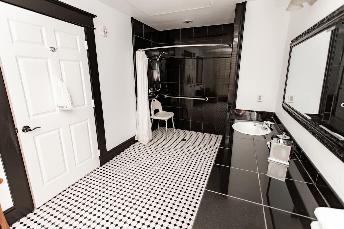 A bathroom with a black and white tiled floor, a white sink, a mirror, and a shower area.