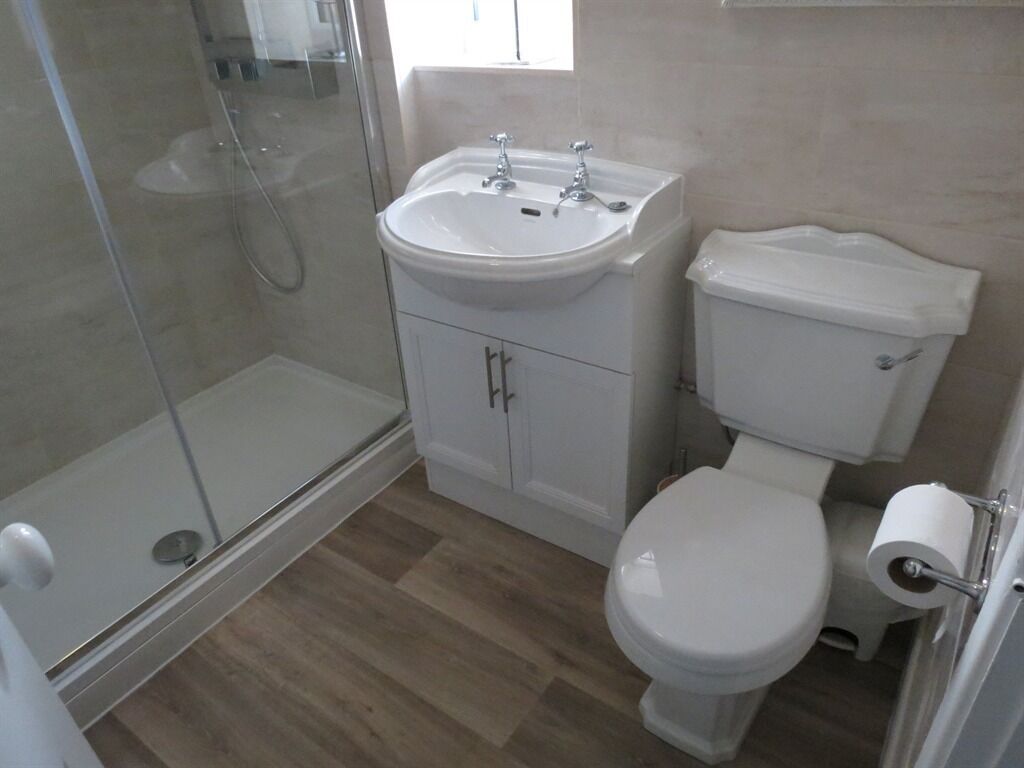Une salle de bain avec une douche à parois de verre, un lavabo blanc doté de deux robinets, des toilettes et un rouleau de papier toilette fixé au mur.