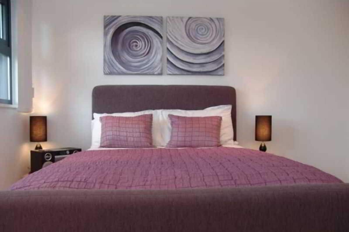 Uma cama com cabeceira, duas luminárias de apoio e duas obras de arte abstratas na parede.