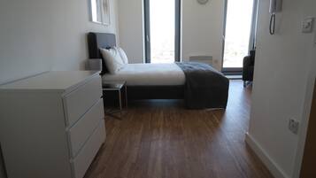 A bedroom with a bed, a desk, a dresser, and a window with a city view.