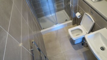 Egy modern fürőszoba üveg válaszfallal ellátott zuhanyzóval, WC-vel és mosdókagylóval.