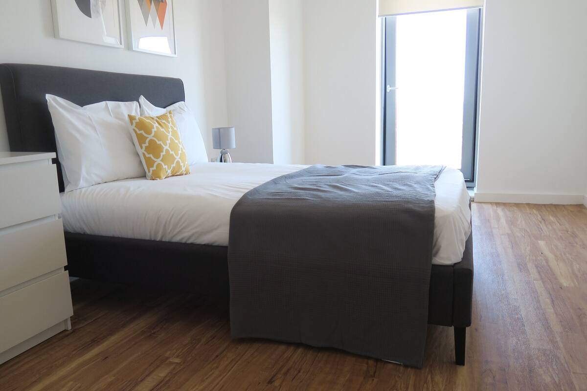Um quarto moderno com uma cama, mesa de cabeceira e criado-mudo.