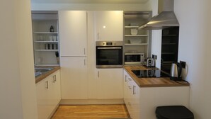 A compact kitchen with white cabinets, a built-in oven, microwave, and a coffee maker on the countertop. - Quay Apartments (Salford)