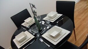 A round dining table set for four with white plates, silverware, and a green vase with a flower arrangement. - Quay Apartments (Salford)