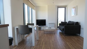 A modern living room with a flat-screen TV, a sofa, a dining table, and a chair.