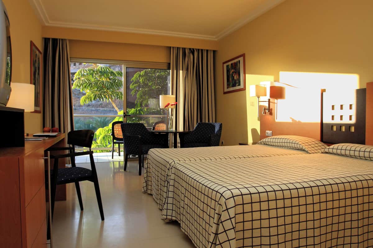 Une chambre d’hôtel avec un lit, un bureau, une chaise et une vue sur la verdure.