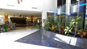 A modern lobby with a reception desk, seating area, and a glass enclosure with plants. - Hotel LIVVO Costa Taurito & Aquapark - All Inclusive (Mogan)