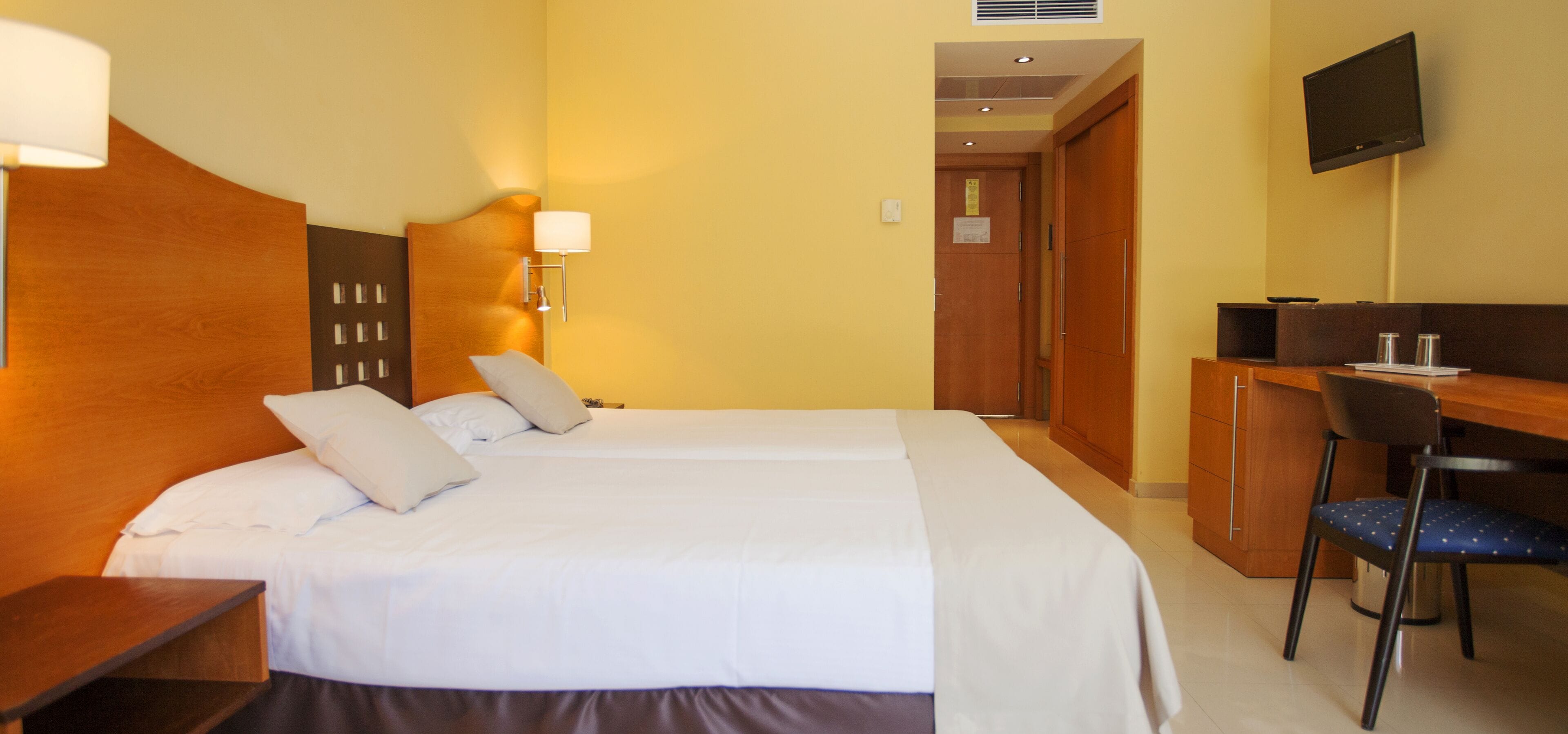 Habitación de hotel con una cama grande, un escritorio con silla, televisión y cabecero de madera.