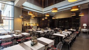 A spacious restaurant with multiple dining tables and chairs, large pendant lights, and a view of the city through large windows. - Golden Tulip Ana Dome (Cluj-Napoca)