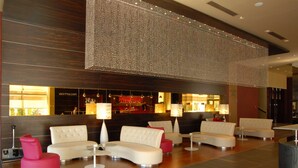 A modern lobby with a bar area, seating arrangements, and a decorative light installation. - Golden Tulip Ana Dome (Cluj-Napoca)