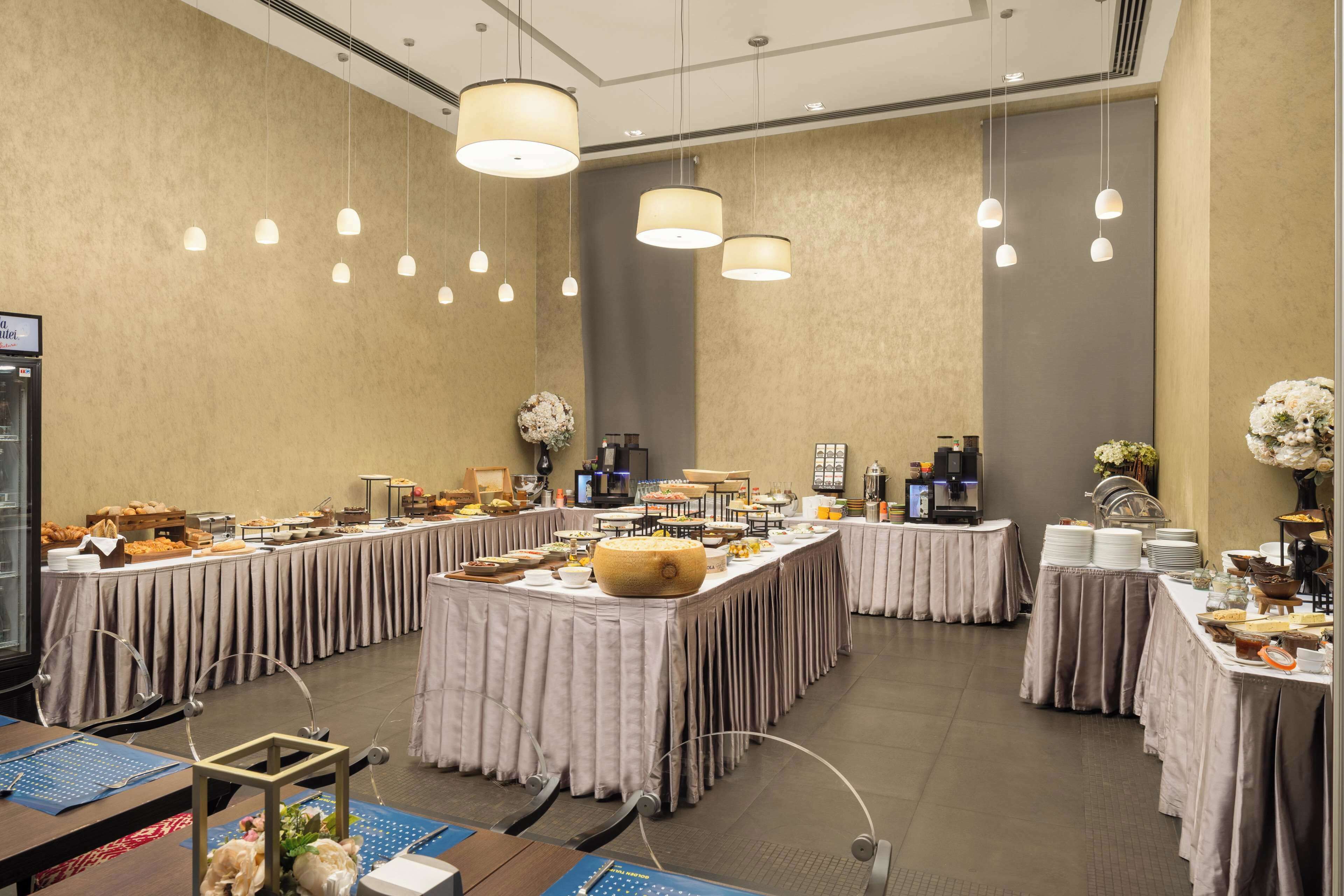 A spacious banquet hall with multiple tables set for a buffet, featuring a variety of food items and a coffee station.