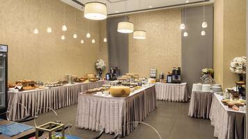 A spacious banquet hall with multiple tables set for a buffet, featuring a variety of food items and a coffee station.