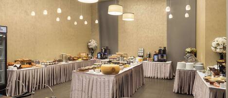 A spacious banquet hall with multiple tables set for a buffet, featuring a variety of food items and a coffee station.