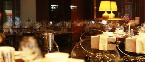 Restaurante con mesas dispuestas para comer, una lámpara al fondo y vistas de la ciudad a través de la ventana.