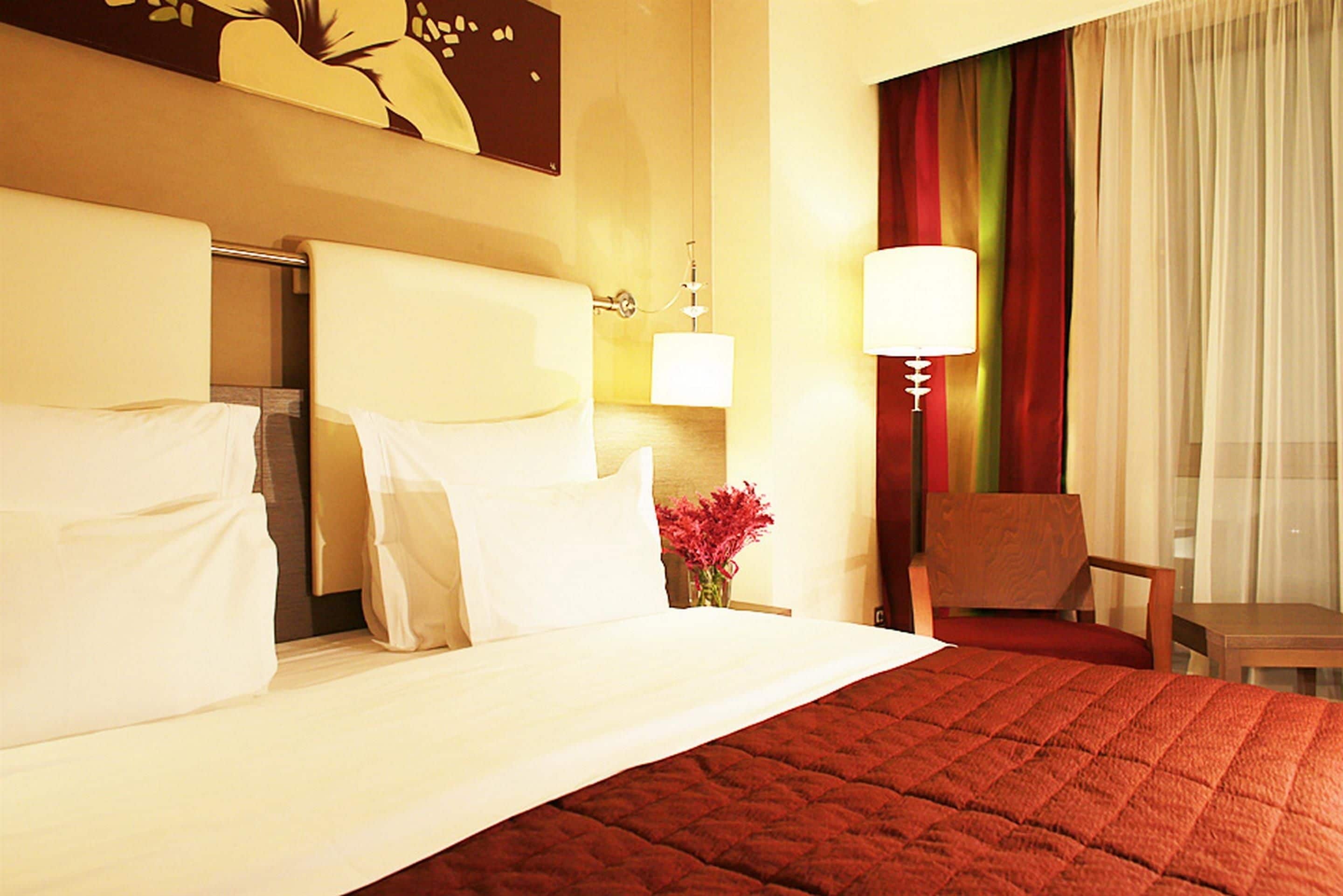 A hotel room with a large bed, a chair, a lamp, and a painting on the wall.