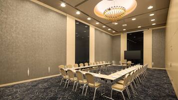 A conference room with a long table, chairs, a chandelier, and a large screen.