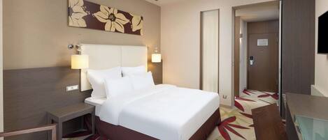 A hotel room with a large bed, bedside tables, a desk, and a mirror.