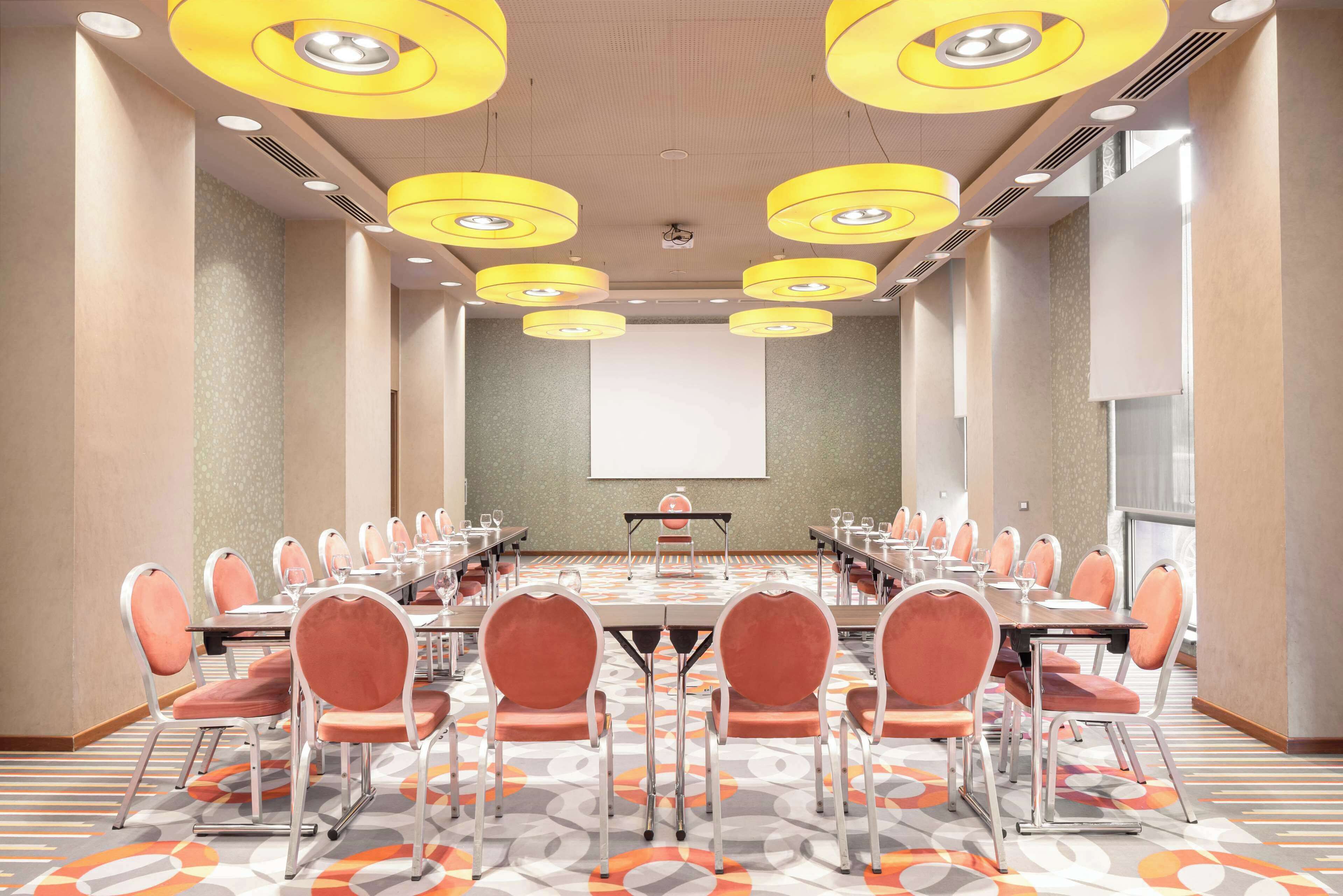 A conference room with a long table, multiple chairs, and a projector screen.