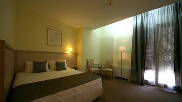 A hotel room with a large bed, two chairs, a table, and a window with curtains.