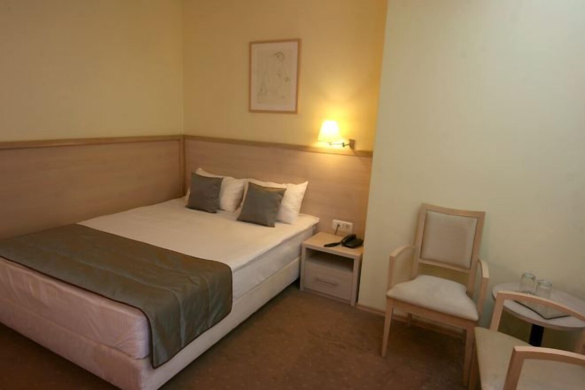 A hotel room with a bed, bedside tables, a chair, and a small table.