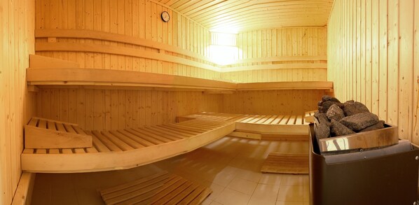 A sauna with wooden benches and a stone-filled container. - Hotel Savoy (Timisoara)