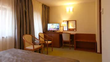 Una camera d'albergo con un letto, una scrivania con un computer, due sedie, una TV e uno specchio.