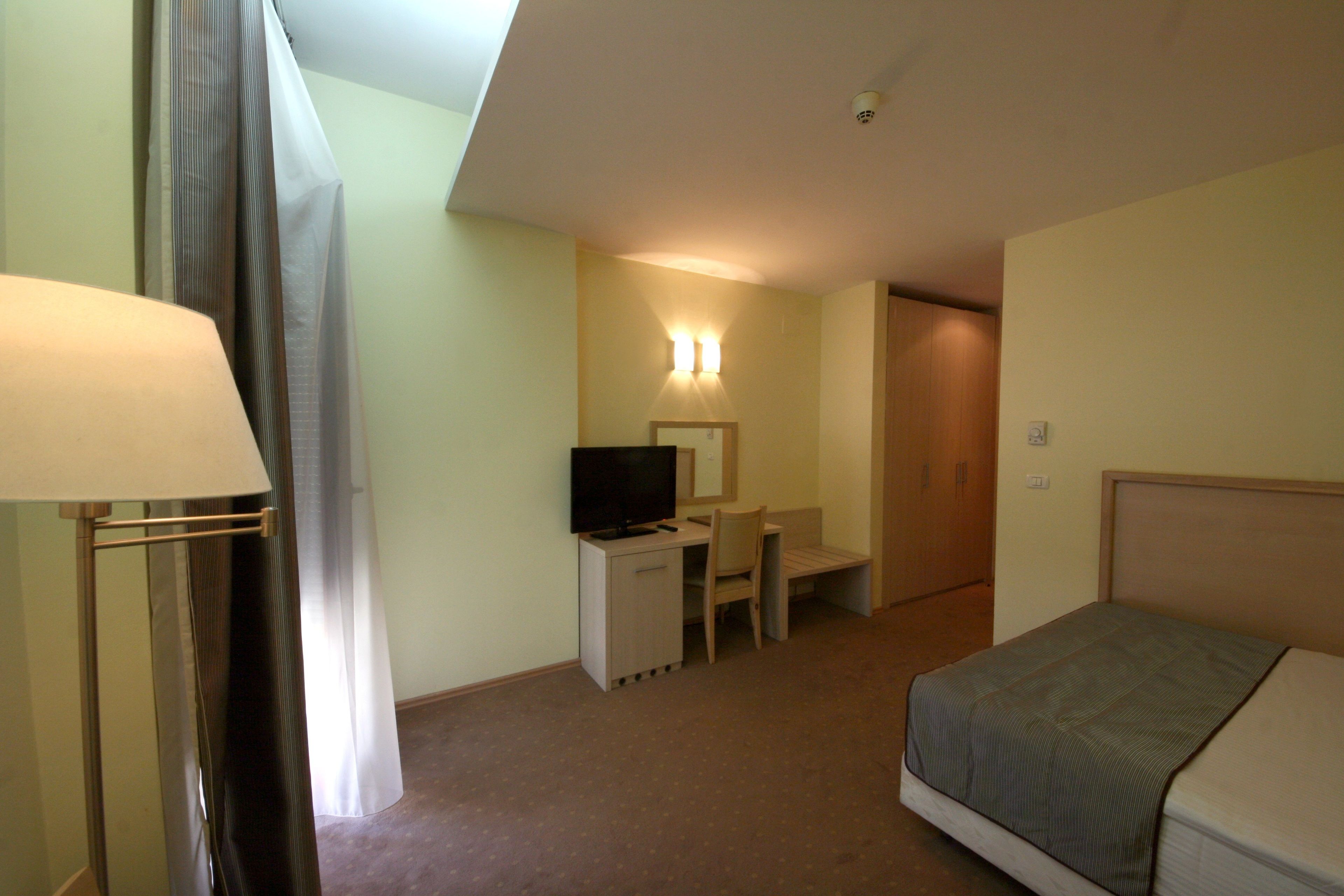 A hotel room with a bed, a desk, a chair, a television, and a lamp.