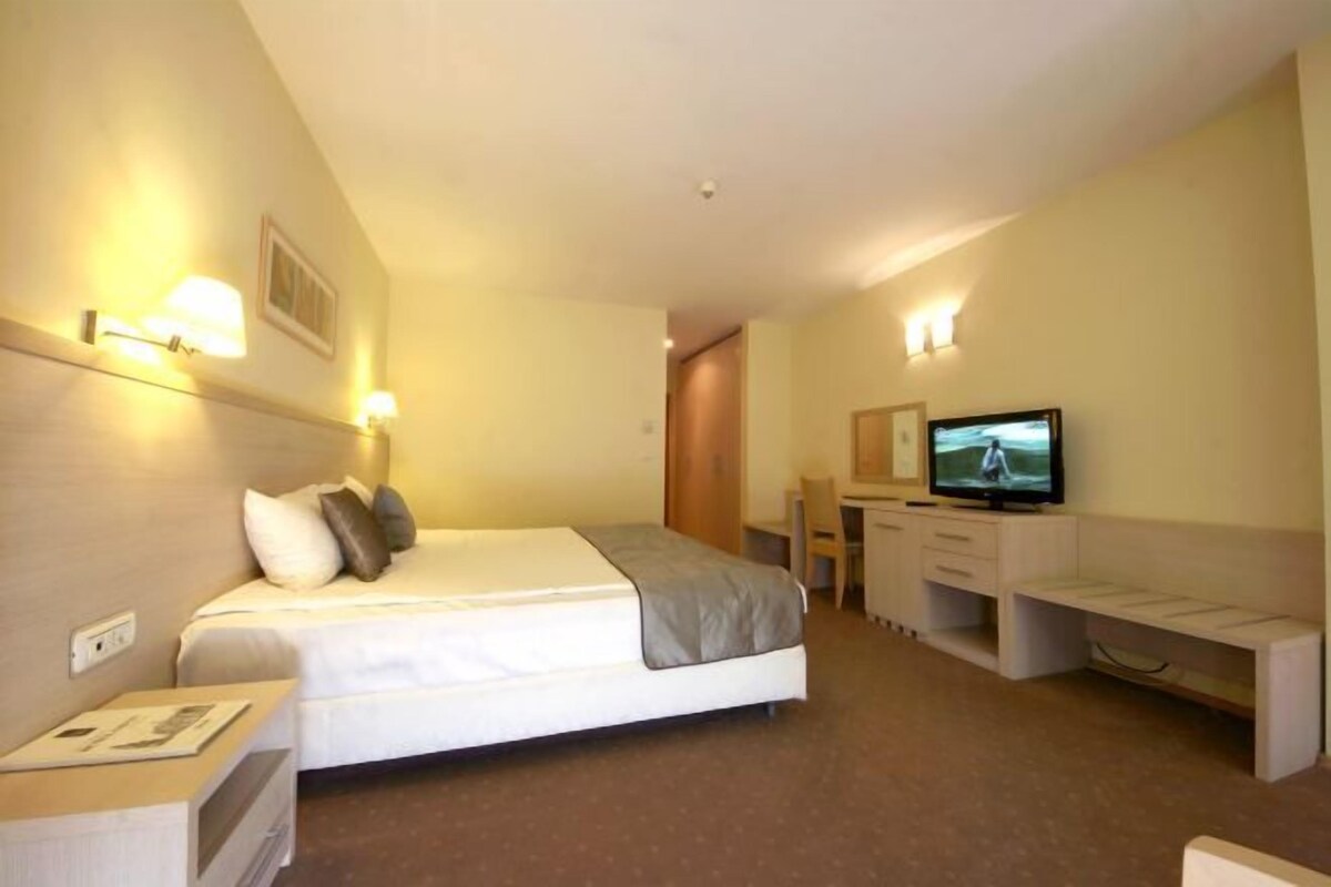 A hotel room with a bed, bedside table, TV, desk, and chair.