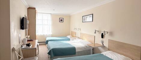 A hotel room with three beds, a desk, a chair, a telephone, and a window.