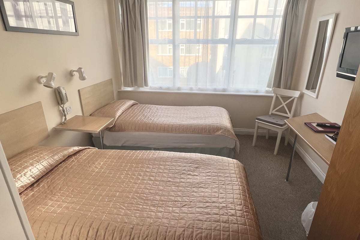Une chambre d’hôtel avec deux lits, un bureau, une chaise, un téléphone et une fenêtre avec des rideaux.