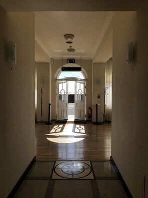 A hallway with a central door leading to an outdoor area, a fire extinguisher, and a ceiling-mounted light fixture.