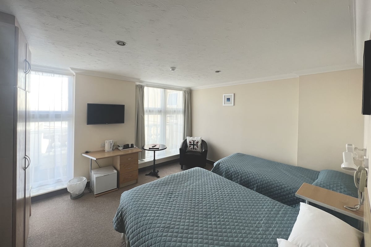 Une chambre d’hôtel avec deux lits, un bureau, une chaise, une télévision et une fenêtre avec des rideaux.