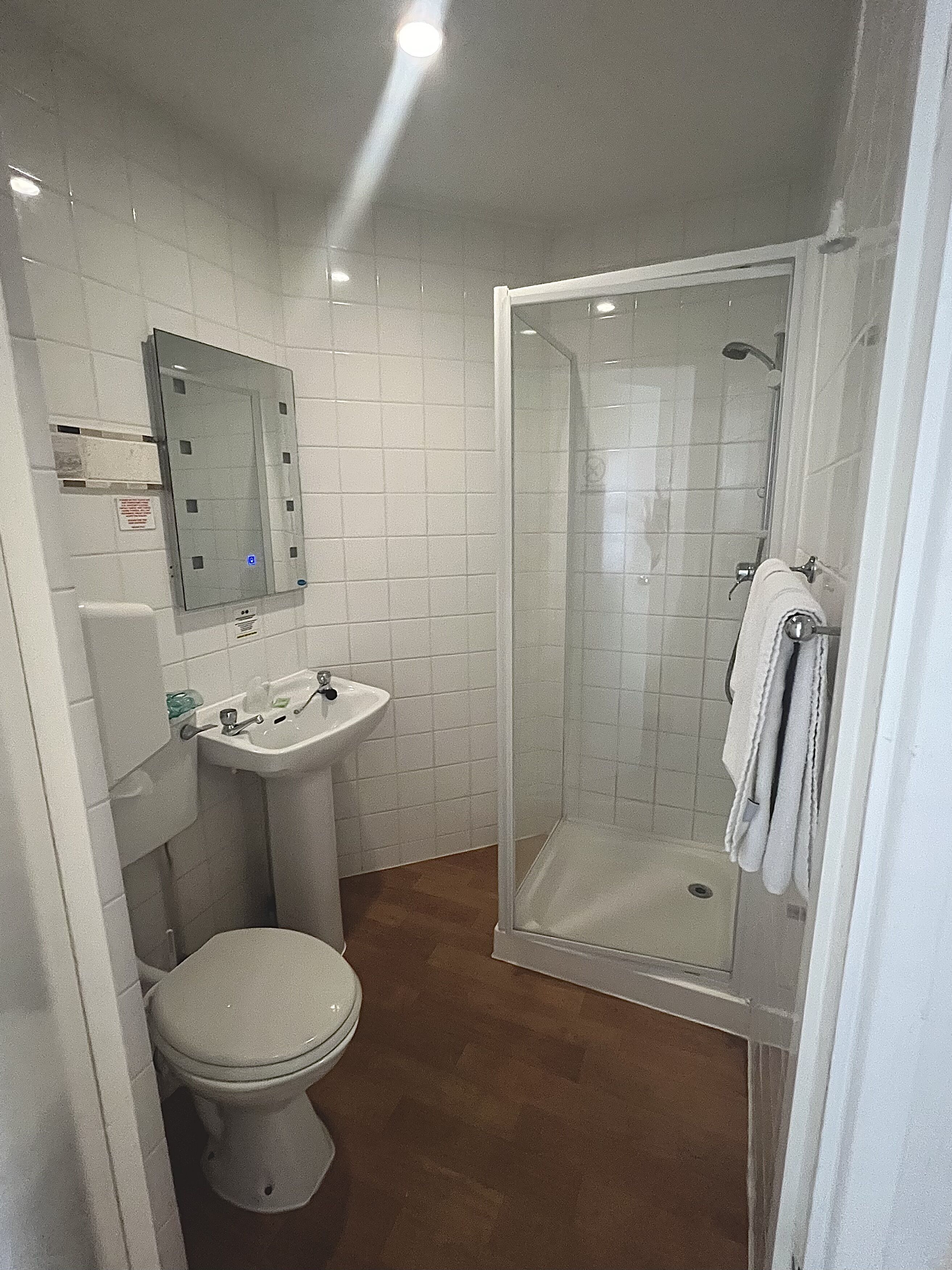 A bathroom with a toilet, sink, mirror, and a glass-enclosed shower.