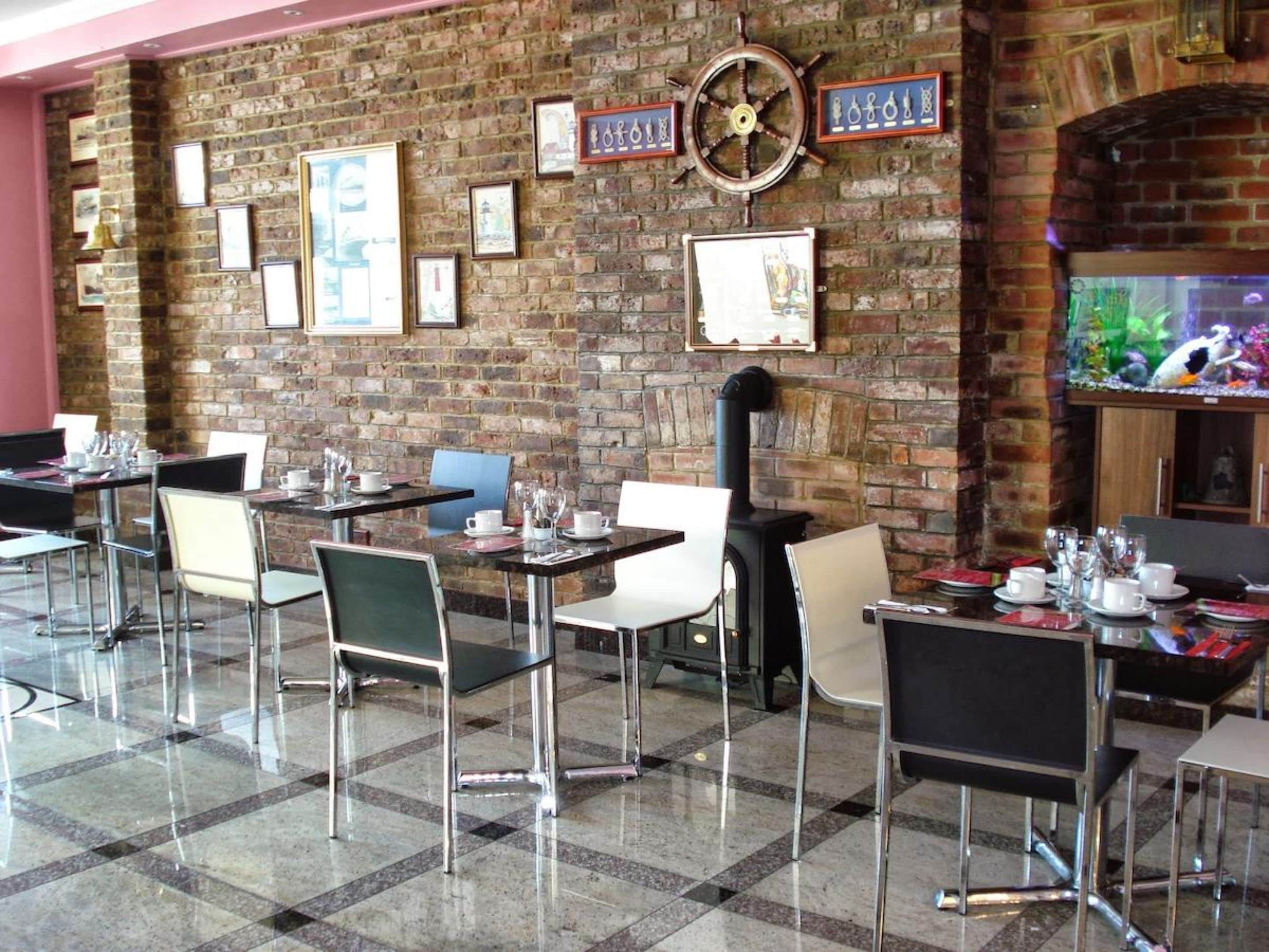 A restaurant with brick walls, framed pictures, a ship's wheel, and a fish tank.