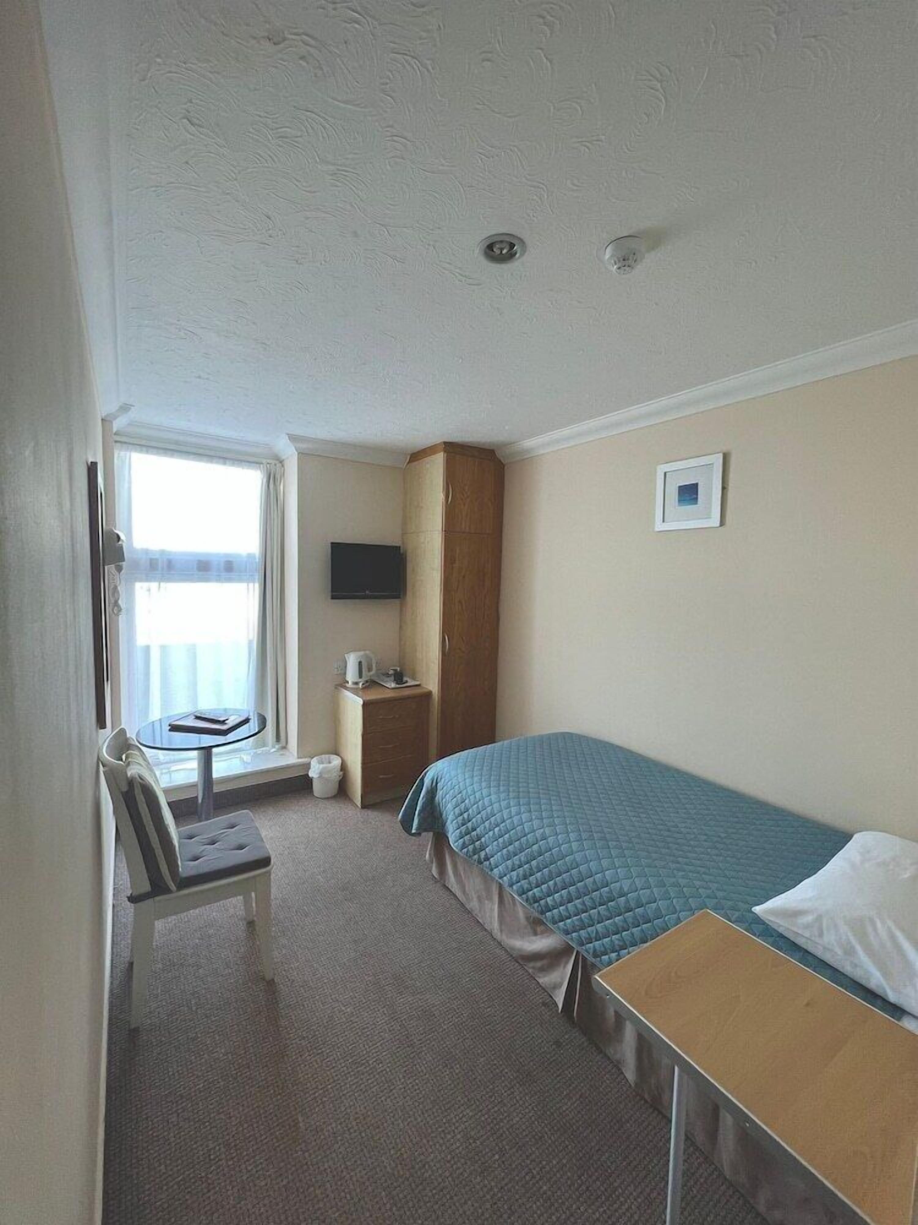 A hotel room with a bed, a desk, a chair, a television, a small cabinet, and a window with curtains.