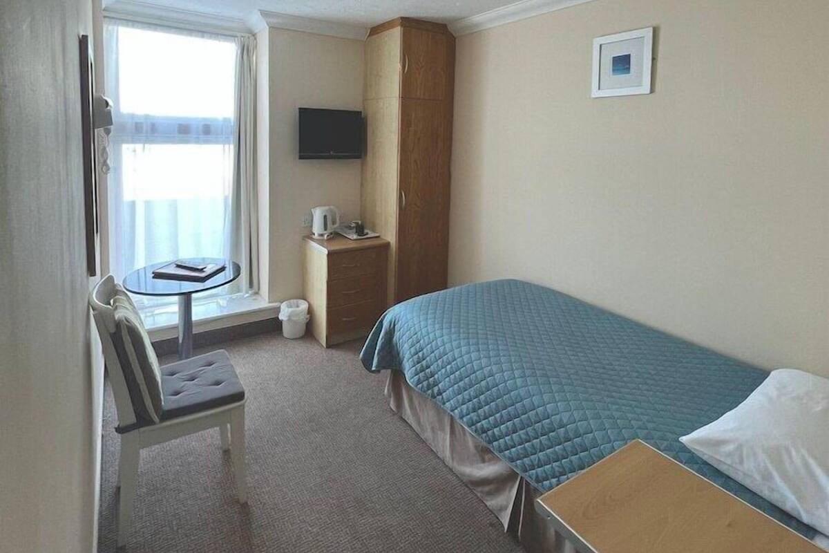 Une chambre d’hôtel comprenant un lit, un bureau, une chaise, une télévision, une petite armoire et une fenêtre avec des rideaux.
