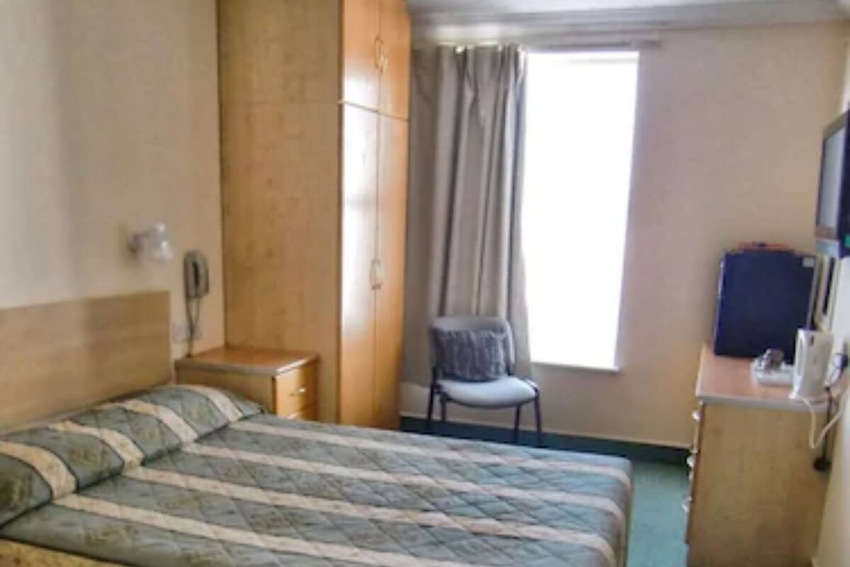 Une chambre d’hôtel comprenant un lit, un bureau, une chaise, une armoire, une fenêtre avec des rideaux et un téléviseur.