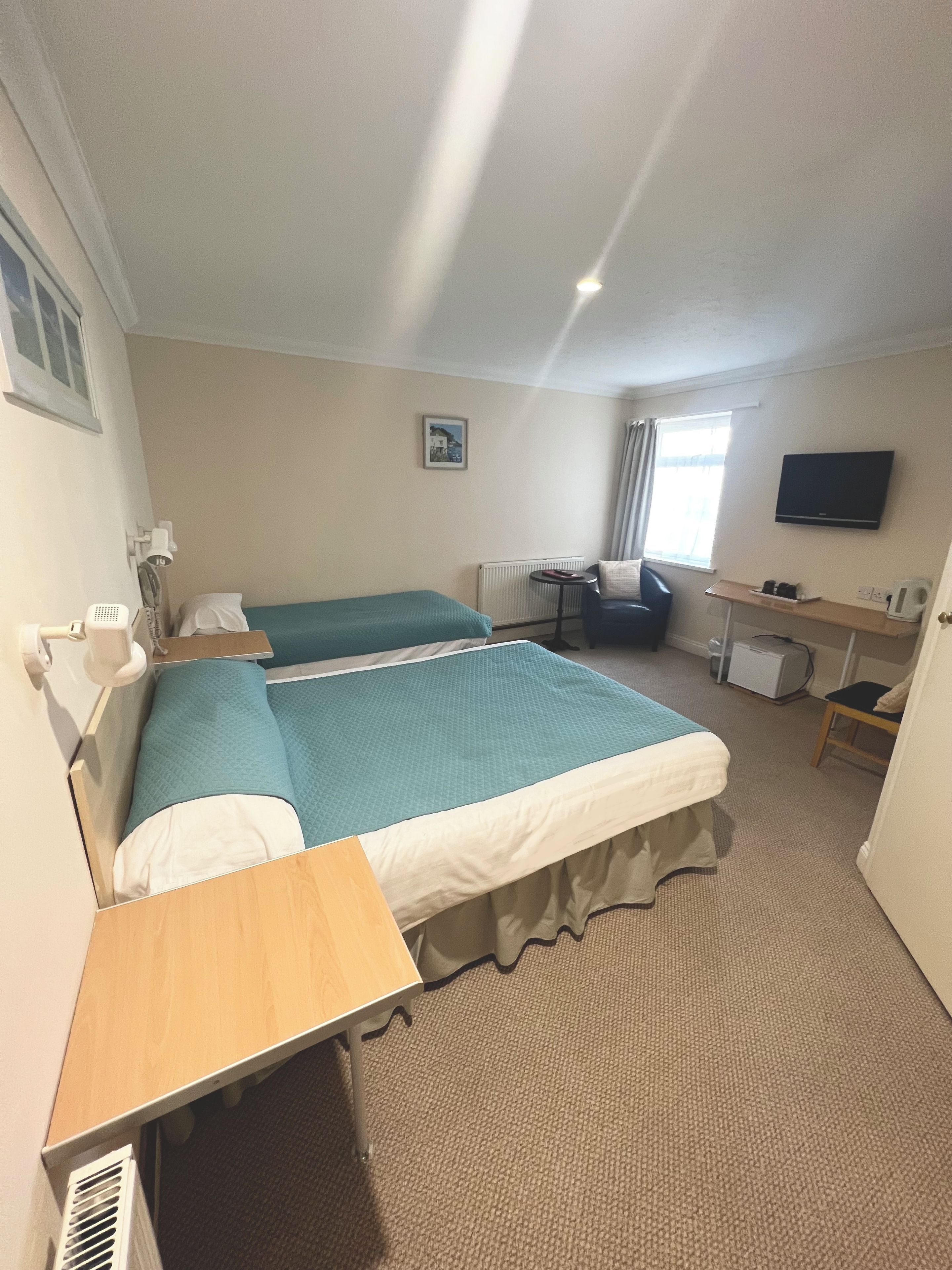 A hotel room with two beds, a desk, a chair, a television, and a window.