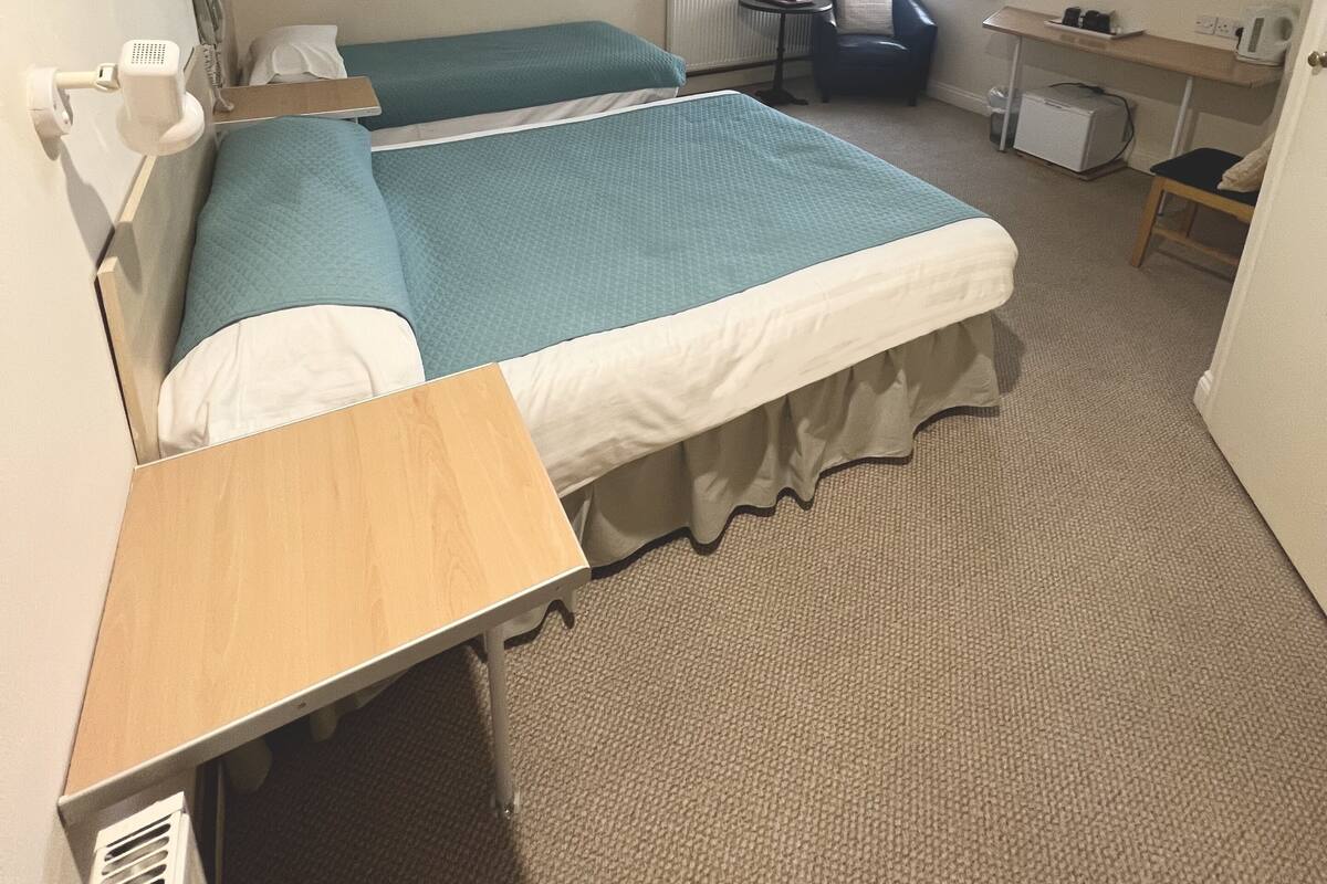 Une chambre d’hôtel avec deux lits, un bureau, une chaise, une télévision et une fenêtre avec des rideaux.
