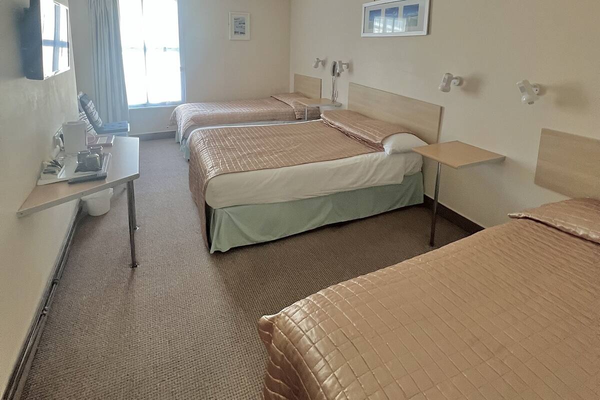 Une chambre d’hôtel avec trois lits, un bureau et une fenêtre avec des rideaux.