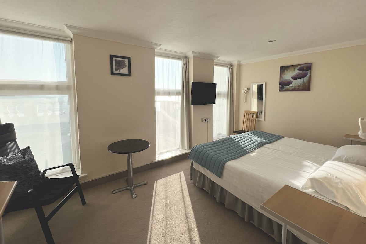 Une chambre d’hôtel comprenant un lit, un bureau, une chaise, une petite table, un téléviseur et une fenêtre avec des rideaux.