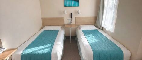 Quarto de hotel com duas camas, uma mesinha, um quadro na parede e janela com cortinas.