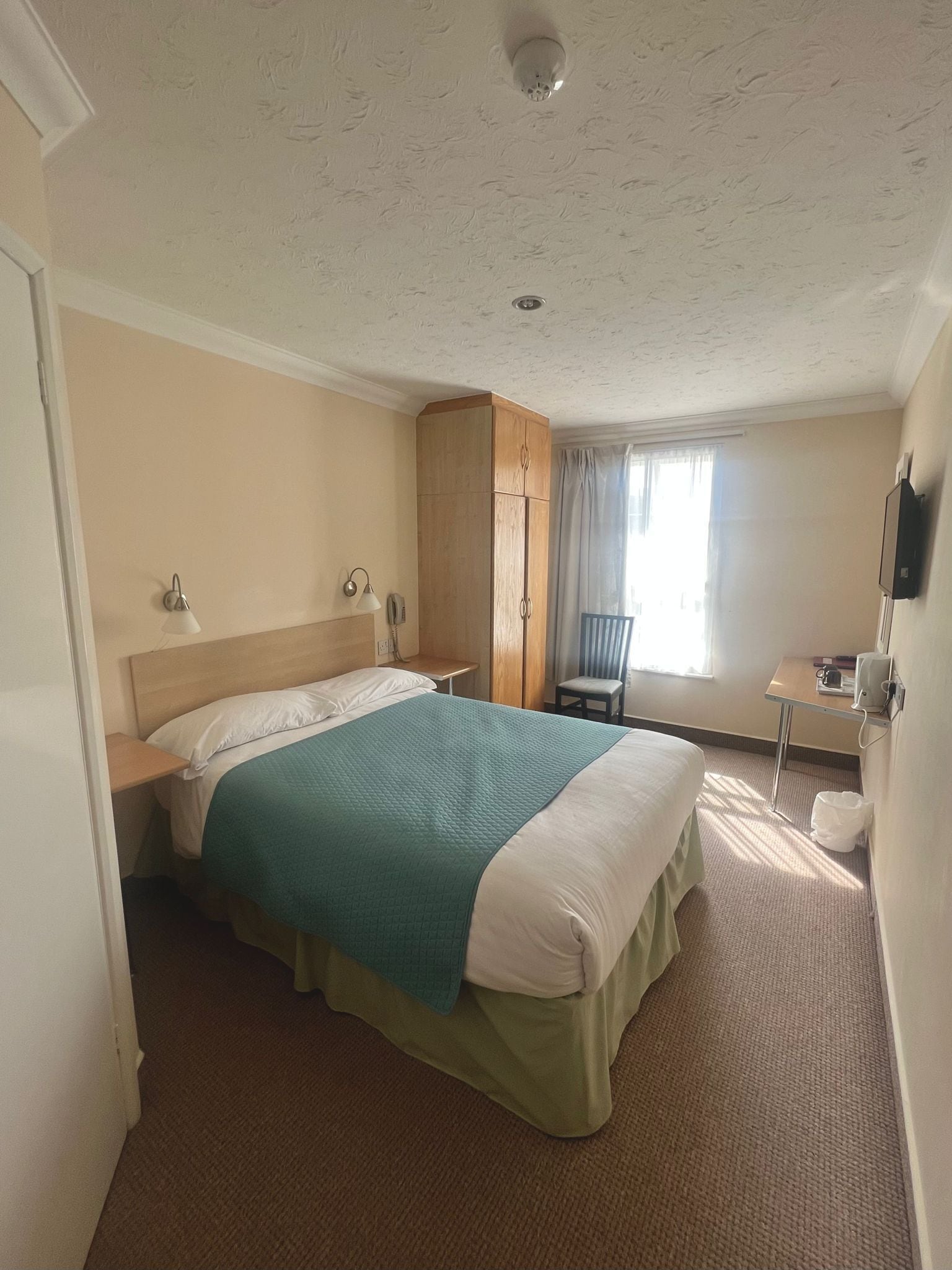 A hotel room with a bed, a wardrobe, a desk, and a chair.