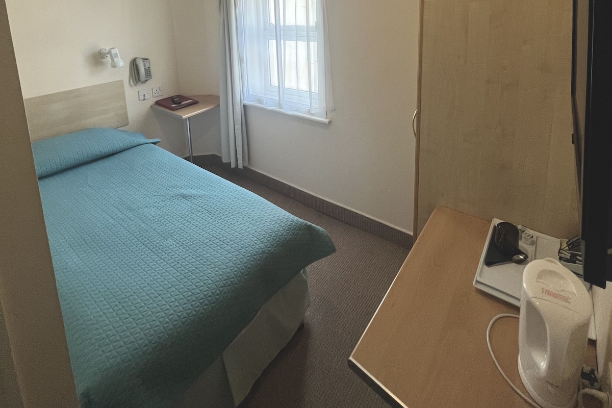 Une chambre d’hôtel équipée d’un lit, d’un bureau, d’un téléphone, d’une fenêtre avec des rideaux et d’un miroir.
