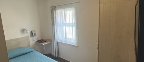 A hotel room with a bed, a desk, a telephone, a window with curtains, and a mirror.