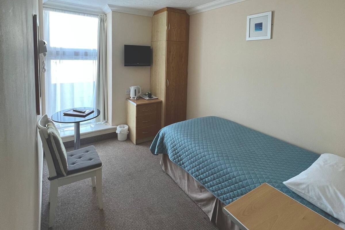 Une chambre d’hôtel comprenant un lit, un bureau, une chaise, une petite table, un téléviseur et une fenêtre avec des rideaux.